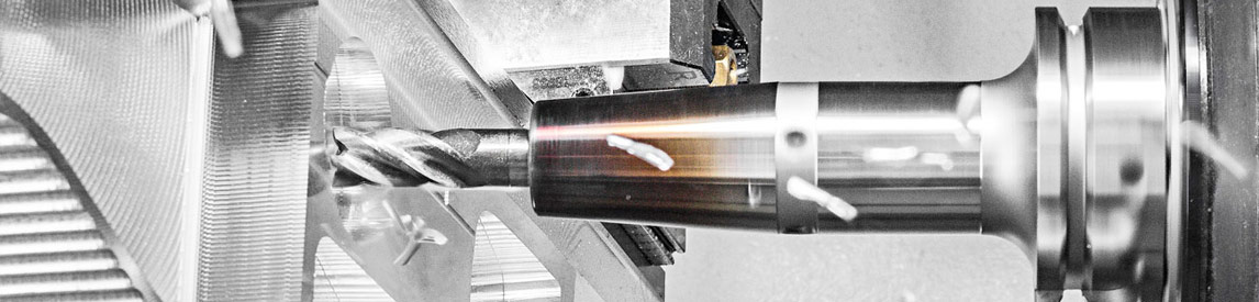Close-up of a CNC lathe cutting a metal cylinder with a cutting tool and metal shavings in the work area.